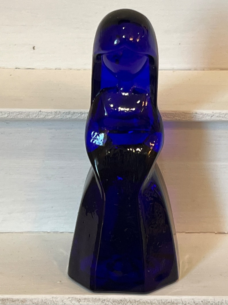 May include: A cobalt blue glass figurine of a woman with a long dress and a simple face.