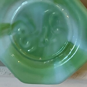 Pu&ograve; includere: Primo piano di un oggetto in vetro verde chiaro con bordo a forma di diamante. Il centro presenta un'indentazione circolare con un motivo a spirale. Il vetro ha una finitura lucida e un sottile effetto marmorizzato bianco.