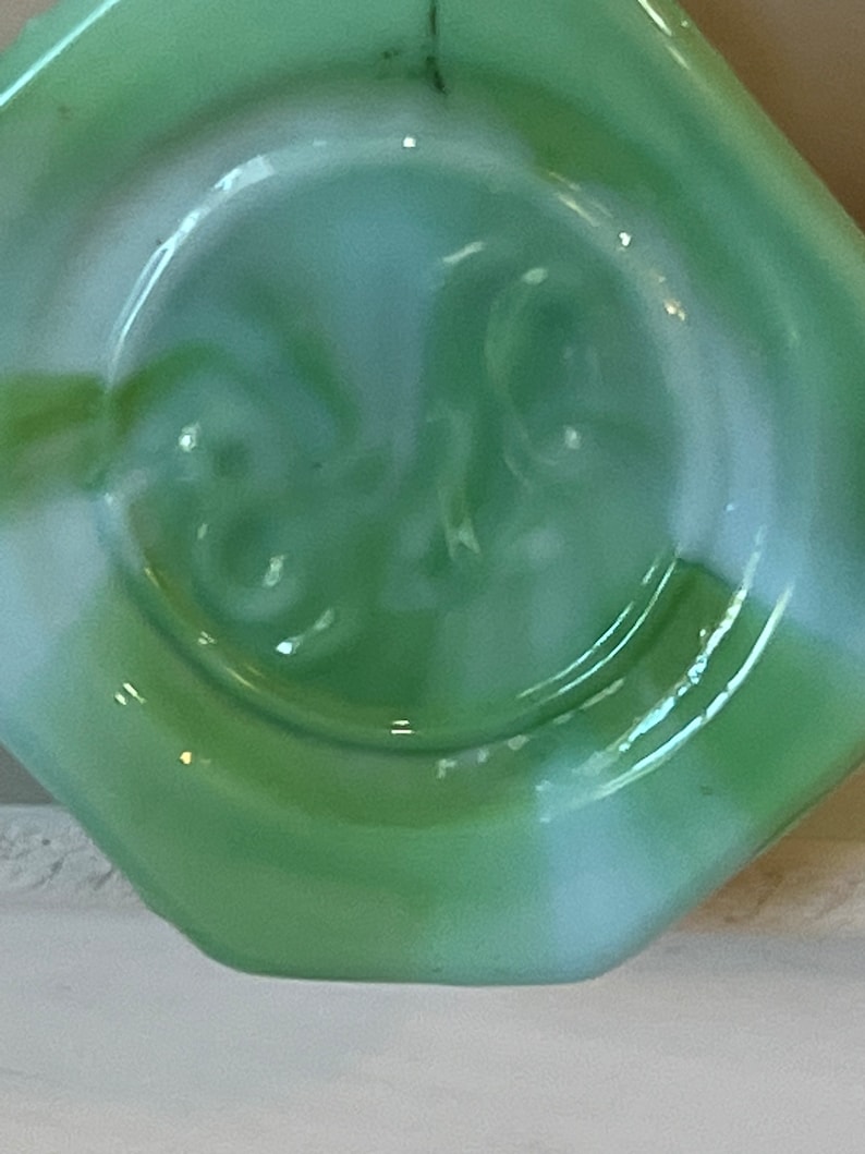 Pu&ograve; includere: Primo piano di un oggetto in vetro verde chiaro con bordo a forma di diamante. Il centro presenta un'indentazione circolare con un motivo a spirale. Il vetro ha una finitura lucida e un sottile effetto marmorizzato bianco.