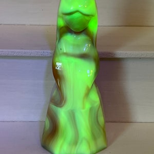 May include: A green and brown glass figurine of a woman with a flowing gown. The figurine is made of swirled glass and has a translucent appearance.