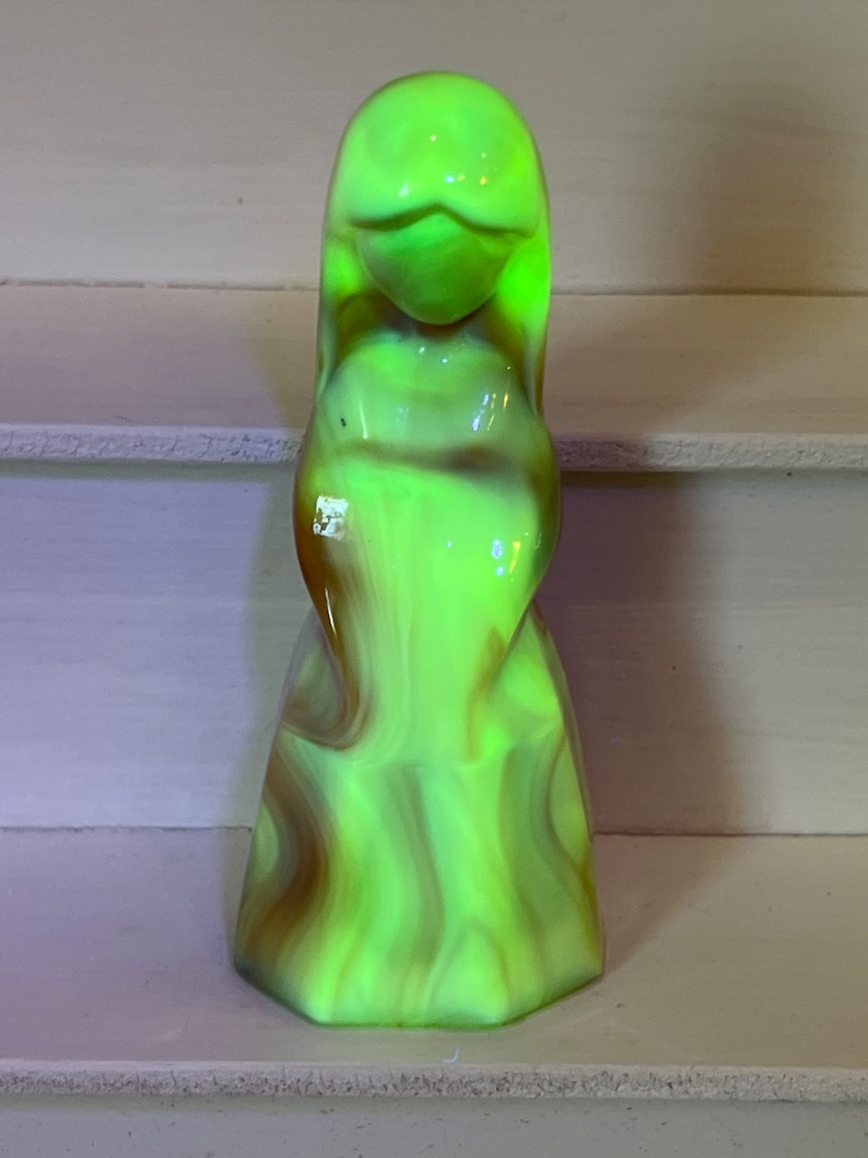 May include: A green and brown glass figurine of a woman with a flowing gown. The figurine is made of swirled glass and has a translucent appearance.