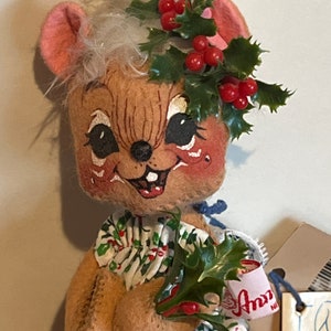 K&ouml;nnte beinhalten: Eine Pl&uuml;schmauspuppe, die einen gr&uuml;nen Stechpalmenkranz mit roten Beeren und ein gr&uuml;n-wei&szlig;es Kleid mit roten Beeren tr&auml;gt. Die Puppe h&auml;lt einen Zweig Stechpalme mit roten Beeren. Die Puppe hat ein Etikett mit der Aufschrift "Ann's".