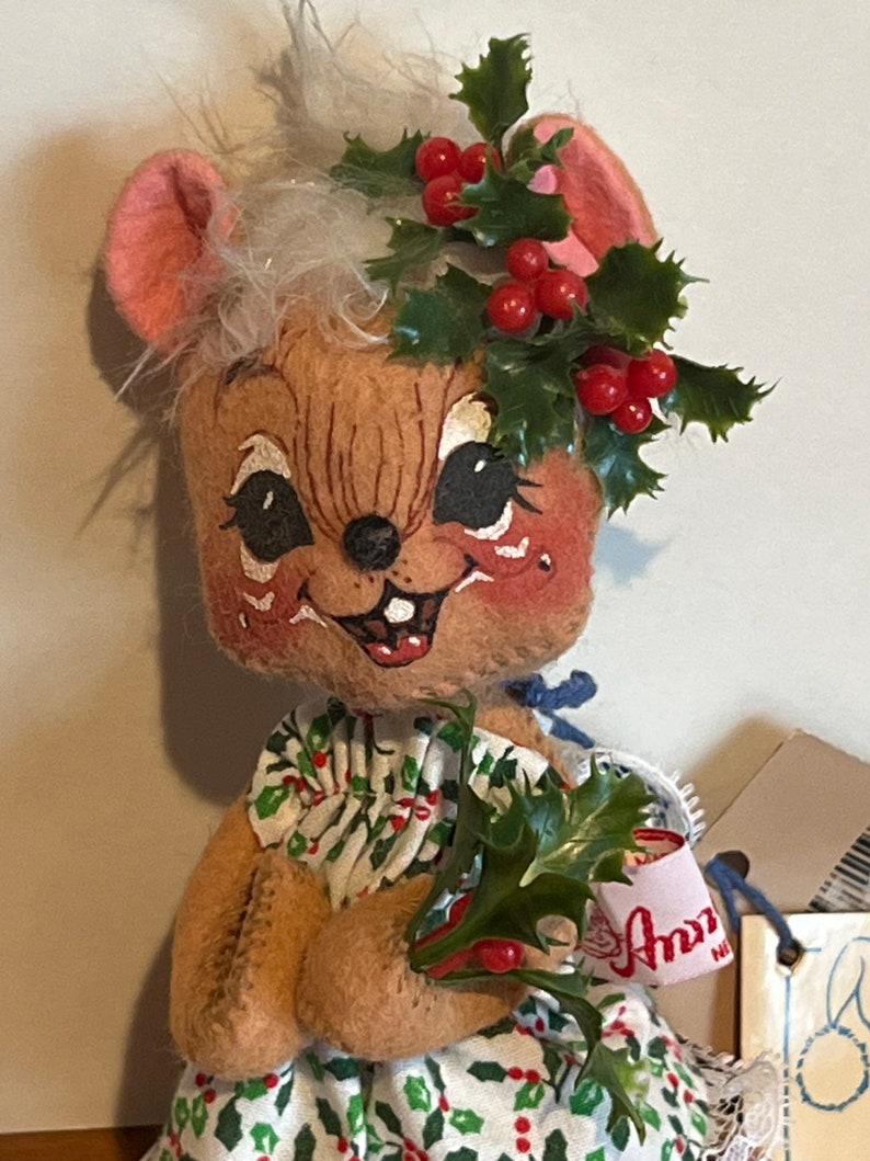 K&ouml;nnte beinhalten: Eine Pl&uuml;schmauspuppe, die einen gr&uuml;nen Stechpalmenkranz mit roten Beeren und ein gr&uuml;n-wei&szlig;es Kleid mit roten Beeren tr&auml;gt. Die Puppe h&auml;lt einen Zweig Stechpalme mit roten Beeren. Die Puppe hat ein Etikett mit der Aufschrift "Ann's".