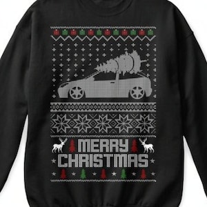 May include: Black Christmas jumper featuring a white car with a Christmas tree on top. The jumper has a white snowflake pattern and the words "Merry Christmas" in red and green.
