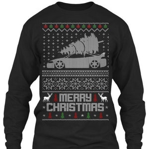 Może przedstawiać: Czarna koszula z długim rękawem z białym wzorem świątecznego swetra. Wzór przedstawia samochód przewożący choinkę, płatki śniegu i napis "Wesołych Świąt".