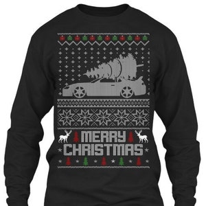 May include: Black long-sleeved Christmas jumper featuring a white silhouette of a car carrying a Christmas tree. The jumper has a red, green and white snowflake pattern and the text "Merry Christmas".