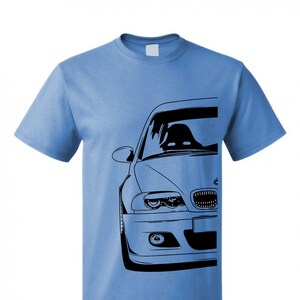 May include: A light blue t-shirt with a black silhouette of a BMW car on the front. The car is facing the viewer and only the front of the car is visible.