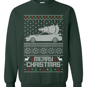 May include: Green Christmas sweater with a white car carrying a Christmas tree. The sweater has a white snowflake pattern and the words "Merry Christmas" in white.