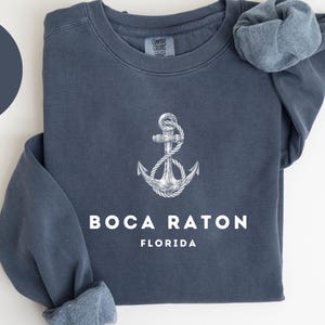 May include: A denim blue sweatshirt with a white anchor design and the text "BOCA RATON FLORIDA". The sweatshirt is a Comfort Colors 1566 style.