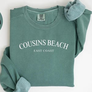 May include: Light green sweatshirt with the text "COUSINS BEACH EAST COAST" in white. The sweatshirt is a Comfort Colors 1566. The image also includes a light green circle with the words "LIGHT GREEN" in black.