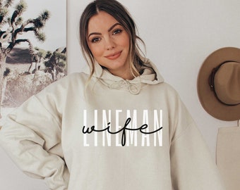 May include: A cream-colored hooded sweatshirt with the text "LINEMAN wife" printed in black on the front.