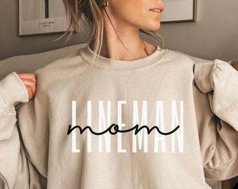 May include: A beige sweatshirt with the text "LINEMAN mom" in black and white lettering.