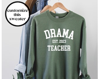 May include: A green sweatshirt with the text "DRAMA EST. 2023 TEACHER" in white.