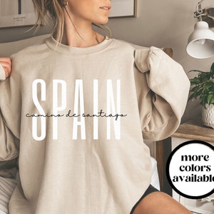 May include: A beige sweatshirt with the text "SPAIN camino de santiago" printed in white on the front.