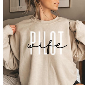 May include: A beige sweatshirt with the text "Pilot wife" in black and white lettering.