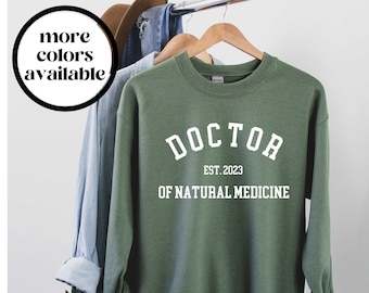May include: A green sweatshirt with the text "DOCTOR EST. 2023 OF NATURAL MEDICINE" in white.