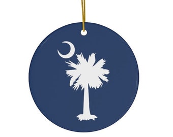 May include: A round, blue ceramic ornament with a white palmetto tree and crescent moon design. This ornament features the state flag of South Carolina.