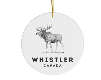 May include: White ceramic ornament with a black and white illustration of a moose and the text "WHISTLER CANADA".