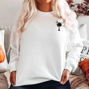 May include: White sweatshirt with a black palm tree and crescent moon design on the left chest.