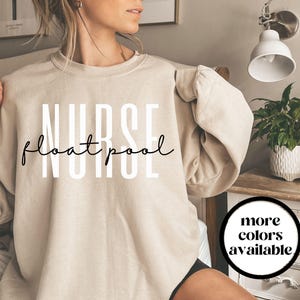 May include: A beige sweatshirt with the words "NURSE float pool" in white and black script. The sweatshirt has long sleeves and a crew neck. A circular graphic on the right says "more colours available".