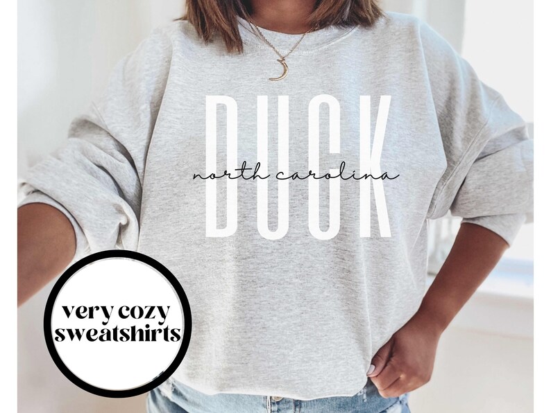 以下が含まれることがあります： グレーのトレーナーに「DUCK north carolina」という白い文字が書かれています。