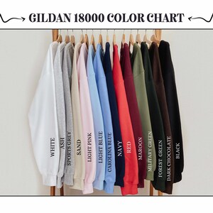 May include: A color chart of Gildan 18000 sweatshirts in various colors, including white, ash, sports grey, sand, light pink, light blue, Carolina blue, navy, red, maroon, military green, forest green, dark chocolate, and black. The text "GILDAN 18000 COLOR CHART" is at the top.