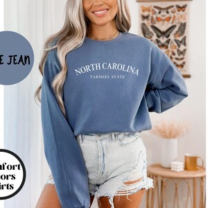 May include: Blue jean colored sweatshirt with the text "NORTH CAROLINA" and "TARHEEL STATE" in white. The sweatshirt is part of the "Comfort Colors Shirts" collection.