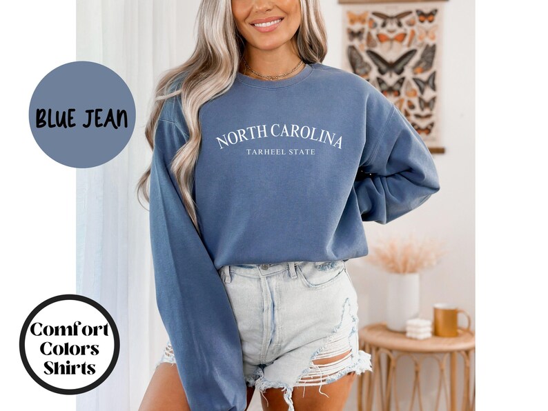 May include: Blue jean colored sweatshirt with the text "NORTH CAROLINA" and "TARHEEL STATE" in white. The sweatshirt is part of the "Comfort Colors Shirts" collection.