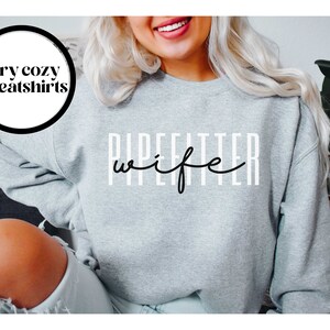 May include: Gray sweatshirt with the text "Pipefitter wife" in black lettering.