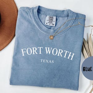 May include: A blue jean t-shirt with the text "FORT WORTH TEXAS" printed in white.