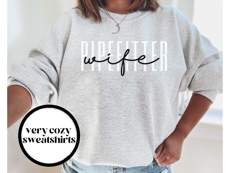 May include: Gray sweatshirt with the text "Pipefitter wife" in black lettering. The text is in a vertical format with white lines behind each letter.