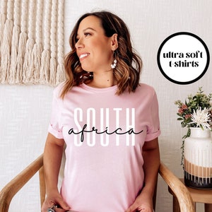 May include: A pink t-shirt with the text "SOUTH AFRICA" in white letters. The t-shirt is advertised as "ultra soft".