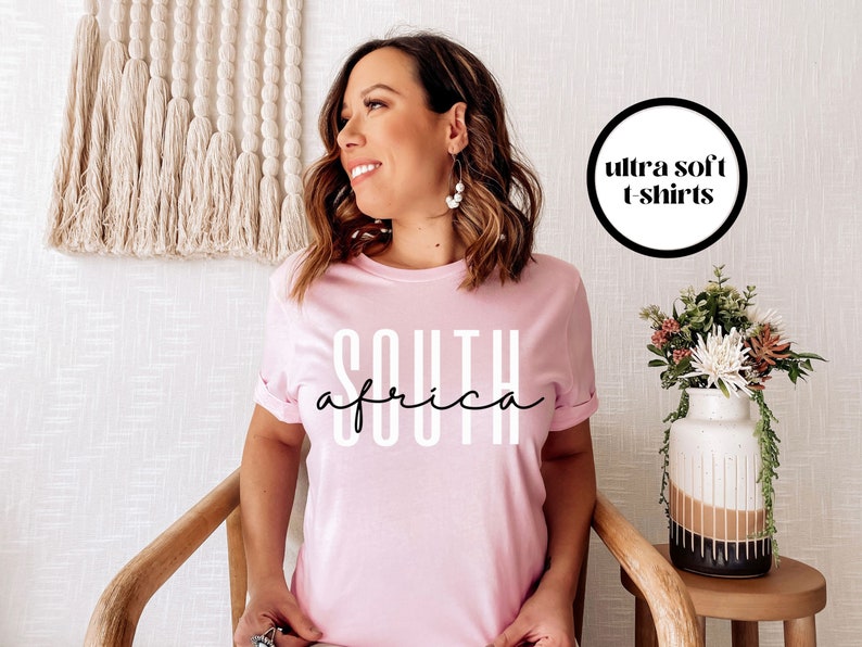 May include: A pink t-shirt with the text "SOUTH AFRICA" in white letters. The t-shirt is advertised as "ultra soft".