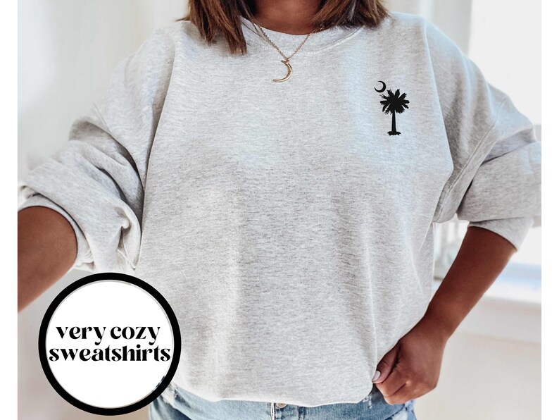 May include: A gray sweatshirt with a black palm tree and crescent moon design. The text "very cozy sweatshirts" is visible in a circle on the bottom left of the image.
