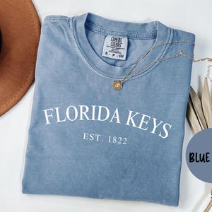 May include: A blue jean t-shirt with the text "Florida Keys Est. 1822" in white.