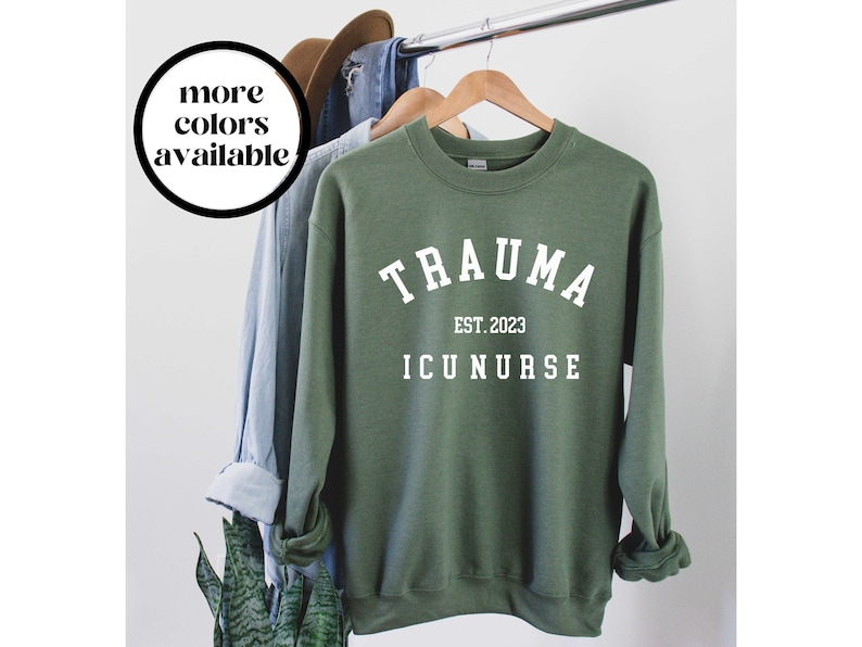 K&ouml;nnte beinhalten: Gr&uuml;ner Pullover mit wei&szlig;em Text, der "Trauma ICU Nurse Est. 2023" lautet.