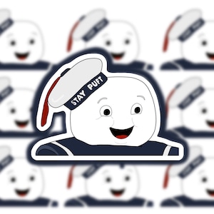 Peut inclure: Un autocollant blanc Stay Puft Marshmallow Man avec un chapeau de marin bleu et une bordure rouge. L'autocollant a un fond blanc et est entouré d'autres autocollants Stay Puft Marshmallow Man.