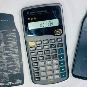 Puede incluir: Una calculadora científica TI-30Xa gris con una pantalla negra que muestra el número 0.01134. La calculadora tiene una variedad de botones, incluidas funciones trigonométricas, logaritmos y exponentes.