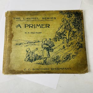 May include: The cover of a vintage book titled "A Primer" from The Laurel Series by W. N. Hailmann and published by C. C. Birchard & Company. The cover features a green and white illustration of children in a field.