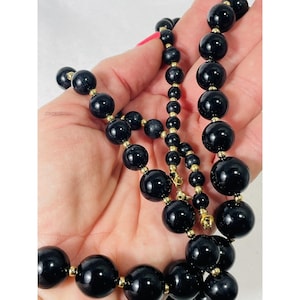 May include: A long black beaded necklace with gold spacers. The beads are large and round.