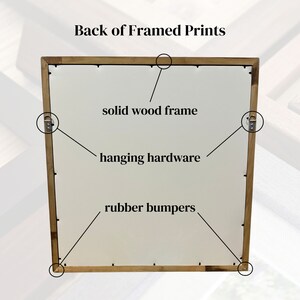 May include: The back of a framed print shows a solid wood frame with hanging hardware and rubber bumpers.