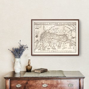 K&ouml;nnte beinhalten: Eine Vintage-Karte der Barbarenk&uuml;ste und der umliegenden Gebiete, gerahmt in einem braunen Holzrahmen. Die Karte ist in Schwarzwei&szlig; gedruckt und zeigt eine Vielzahl von geografischen Merkmalen, darunter St&auml;dte, Fl&uuml;sse und Berge. Der Titel der Karte lautet "I BARBARIAE ET BILEDVLGERID NOVA DESCRIPTIO".