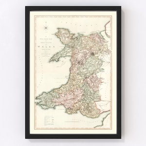 May include: An antique map of Wales, printed in black, red, green, and brown ink on cream paper. The map shows the counties of Wales, with their names and boundaries. The map is framed in a black frame.