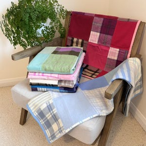 May include: A stack of patchwork blankets in various colours and patterns, including pink, blue, green, and white, are arranged on a wooden chair with a light grey cushion.