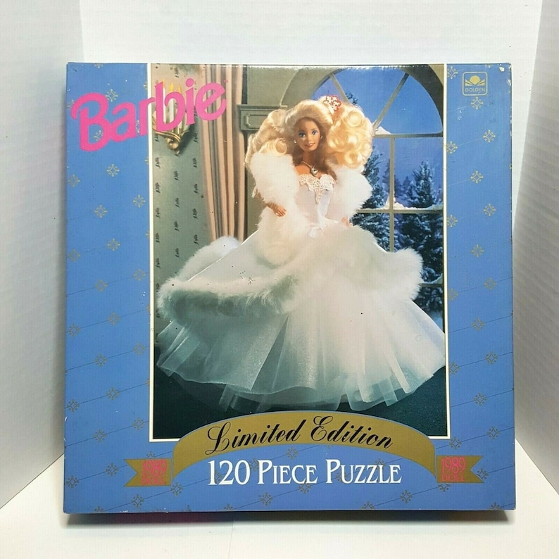 May include: A 120-piece limited edition Barbie puzzle featuring a Barbie doll wearing a white gown with a fur trim and a crown. The background is a snowy winter scene.