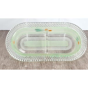 Könnte beinhalten: Eine geteilte Servierplatte aus klarem Glas mit einem strukturierten Rand. Die Platte hat eine hellgrüne Tönung und ein florales Design in Grün und Orange.