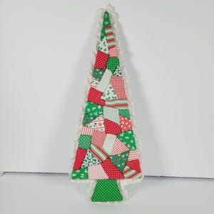 May include: A handmade patchwork Christmas tree wall hanging. The tree is made of red, green, and white fabric scraps and has a white ruffled border.