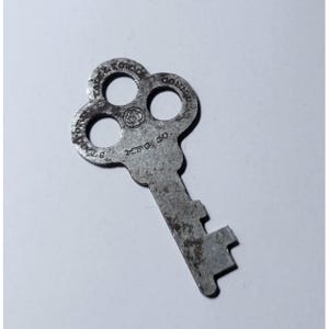 Könnte beinhalten: Ein verwitterter, metallener Schlüssel mit einem kleeblattförmigen Kopf und einem rechteckigen Bart. Der Schlüssel ist mit dem Text "STANLEY WORKS, NEW BRITAIN, CONN. MFG. CO." versehen und hat drei kreisförmige Löcher.