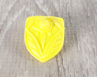 May include: A yellow plastic shield with a sun design. The shield is a toy accessory.