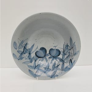 May include: A round ceramic bowl with a light grey speckled finish. The interior features hand-painted blue botanical illustrations of two pomegranate-like fruits surrounded by numerous slender leaves, rendered in varying shades of blue ink.